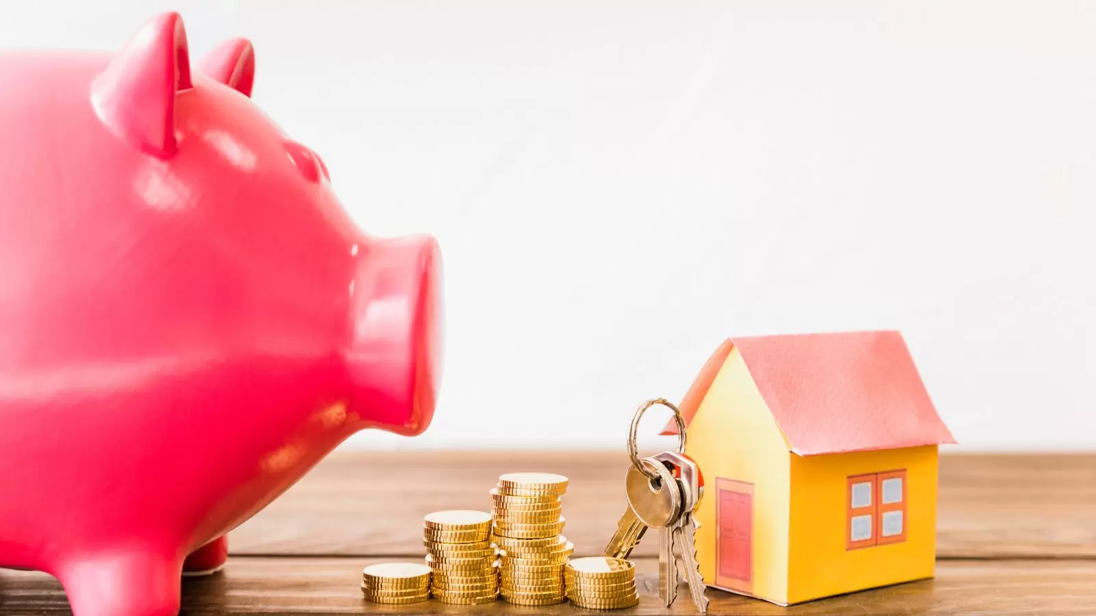 Porquinho, moedas e casa com chaves em cima de mesa
