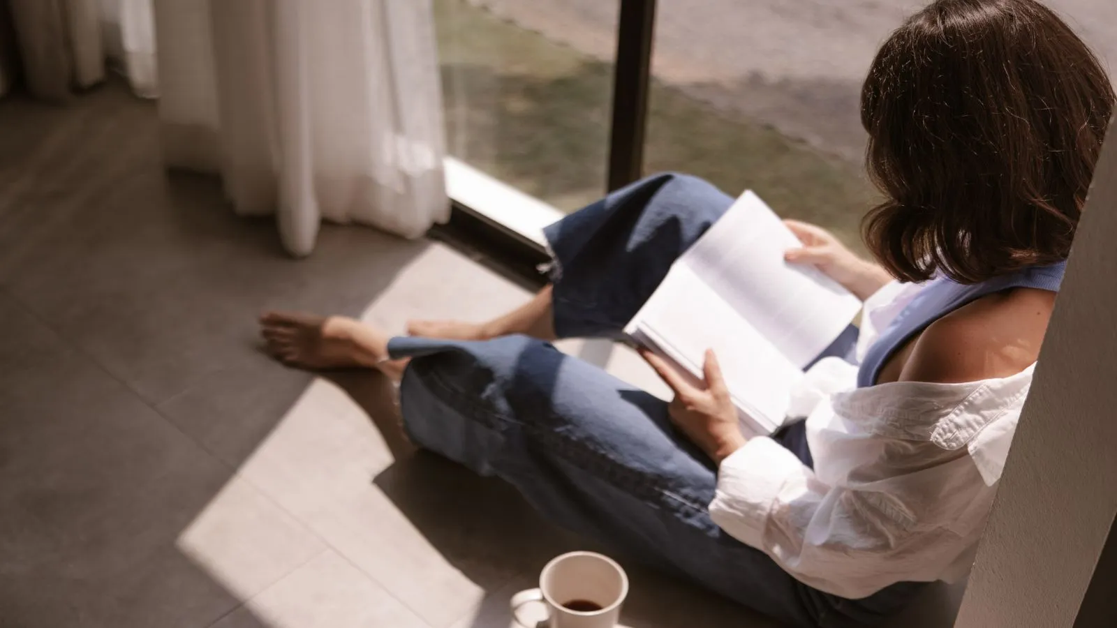 Mulher lendo livro perto de janela