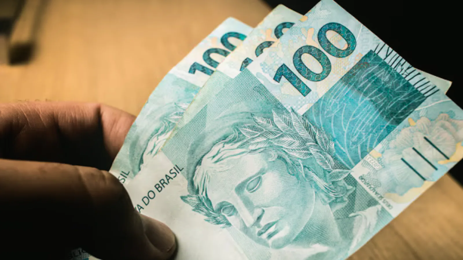 Homem segurando notas de cem reais
