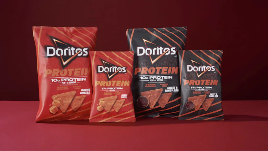 Quatro embalagens de Doritos Protein dispostas lado a lado sobre fundo vermelho. Os pacotes variam entre as cores vermelha e preta e destacam sabores como Nacho Cheese e Sweet Tangy BBQ, al&eacute;m da informa&ccedil;&atilde;o de teor de prote&iacute;na por por&ccedil;&atilde;o.