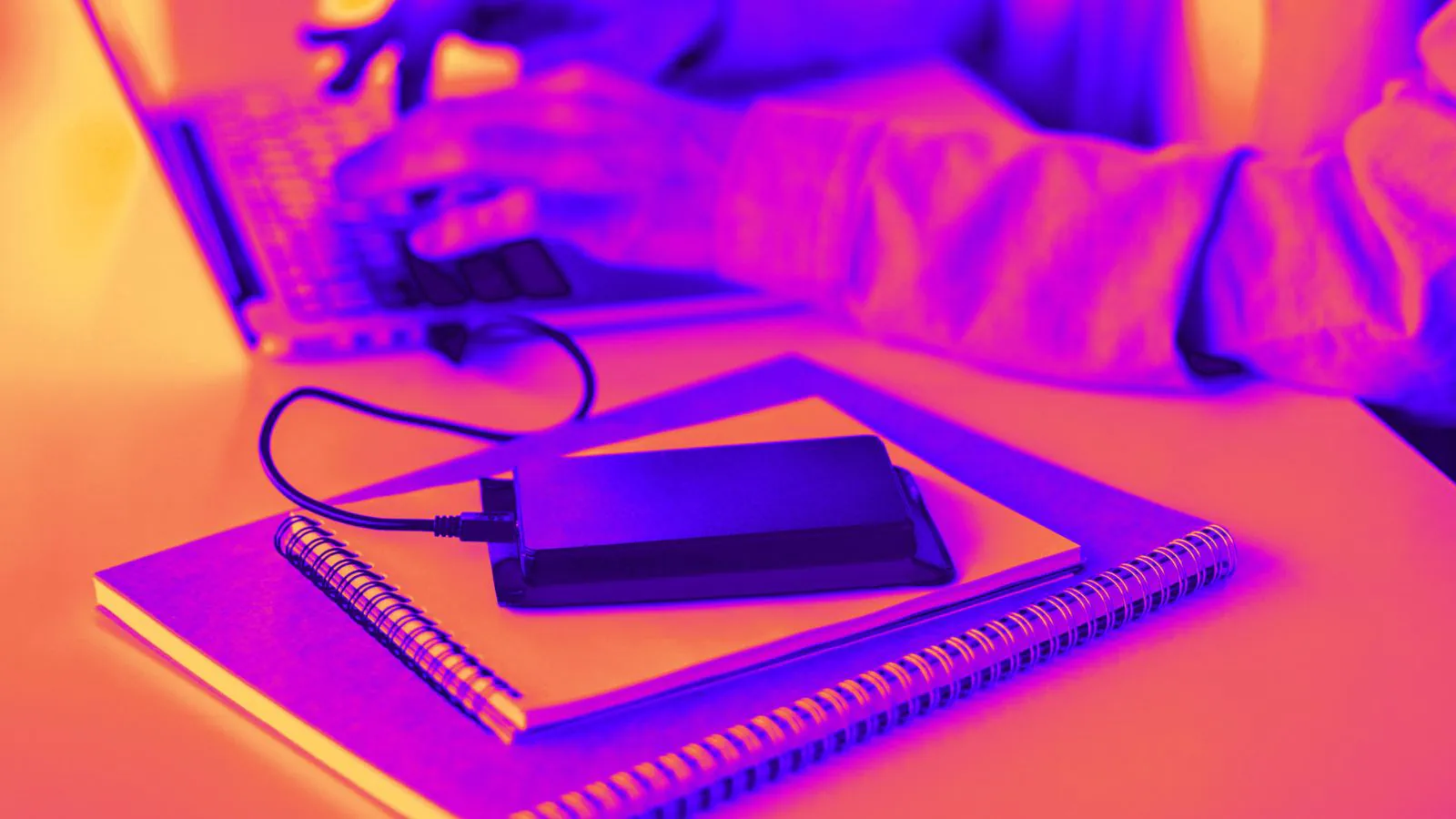 Mulher no computador enquanto se celular carrega em um carregador portatil