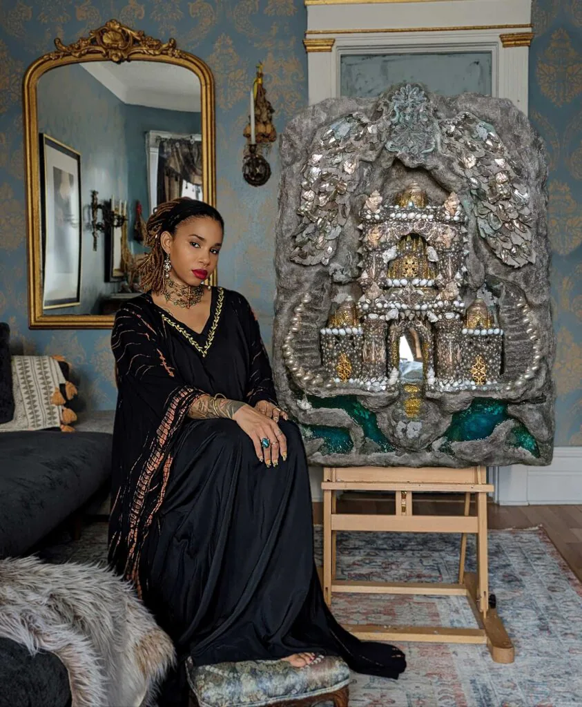 A artista haitiana Fabiola Jean-Louis posa ao lado de uma escultura ornamentada com pérolas e elementos metálicos