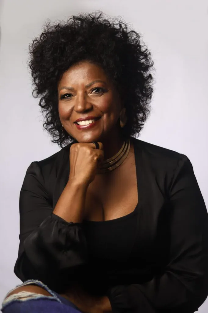 Retrato da escritora brasileira Sandra Menezes sorrindo, com a mão apoiada no queixo