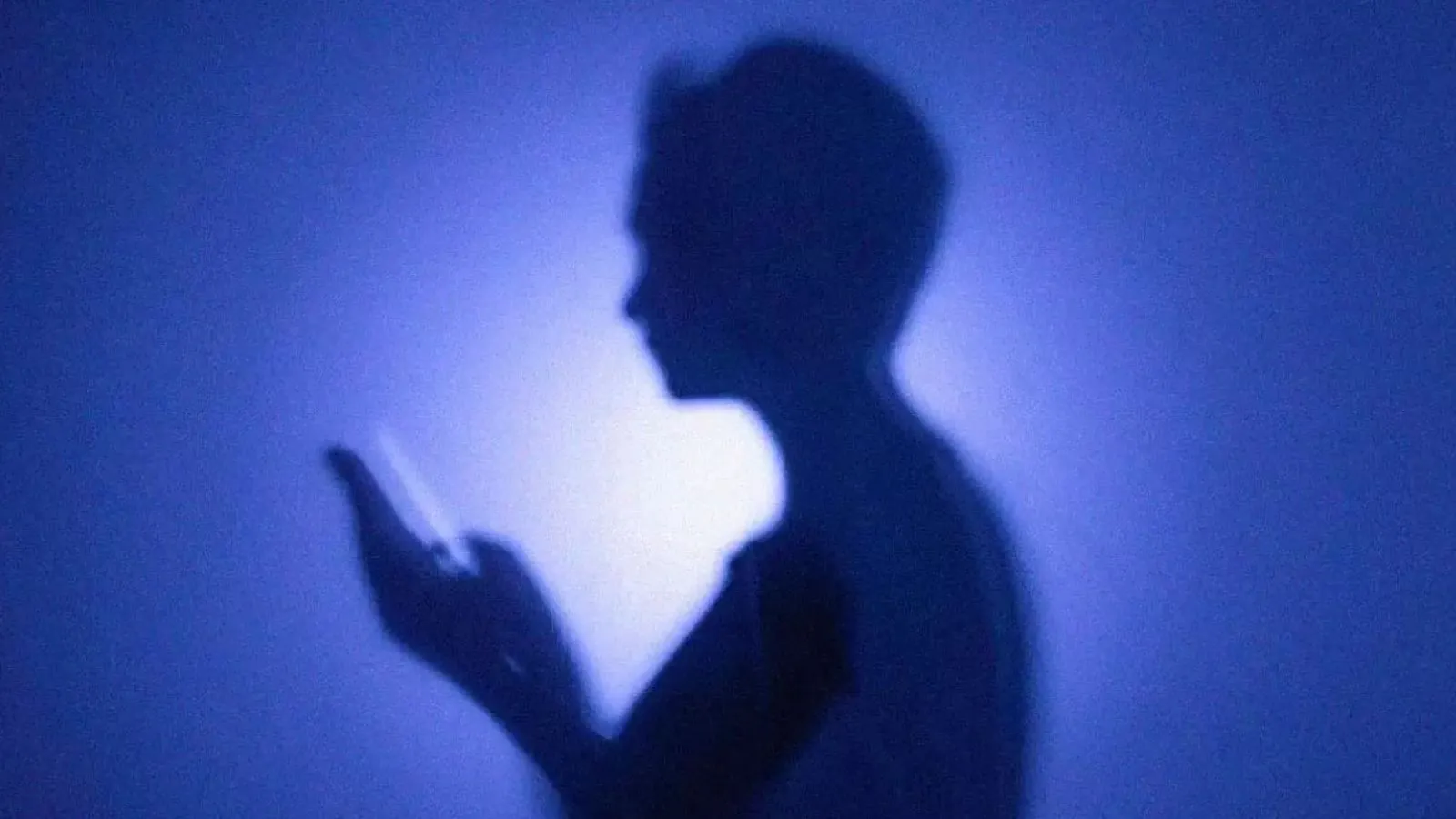Silhueta de uma pessoa segurando um celular nas mãos
