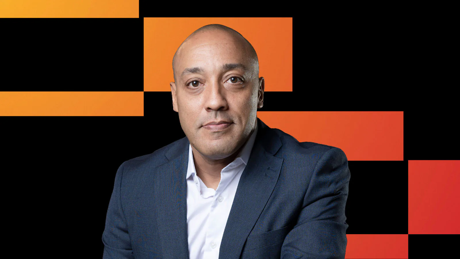 Denis Tassitano, novo CEO da Swile Brasil, veste terno escuro e camisa branca diante de um fundo geométrico preto e laranja.