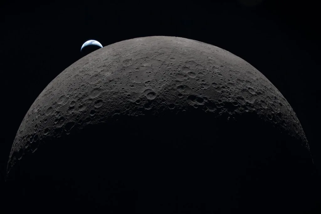 Superf&iacute;cie craterada da Lua com a Terra aparecendo ao fundo no espa&ccedil;o
