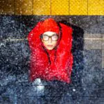 Pessoa usa colete salva-vidas vermelho sob chuva intensa em uma estação de metrô.