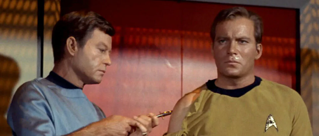 Dr. McCoy aplica uma inje&ccedil;&atilde;o sem agulha no bra&ccedil;o do capit&atilde;o KirkDr. McCoy aplica uma inje&ccedil;&atilde;o sem agulha no bra&ccedil;o do capit&atilde;o Kirk