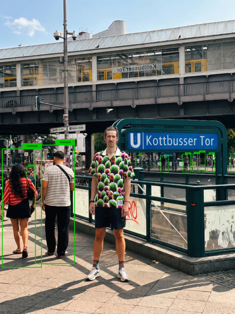 Simon Weckert usa camisa colorida diante da esta&ccedil;&atilde;o Kottbusser Tor, em Berlim, enquanto um sistema de IA identifica outros pedestres.
